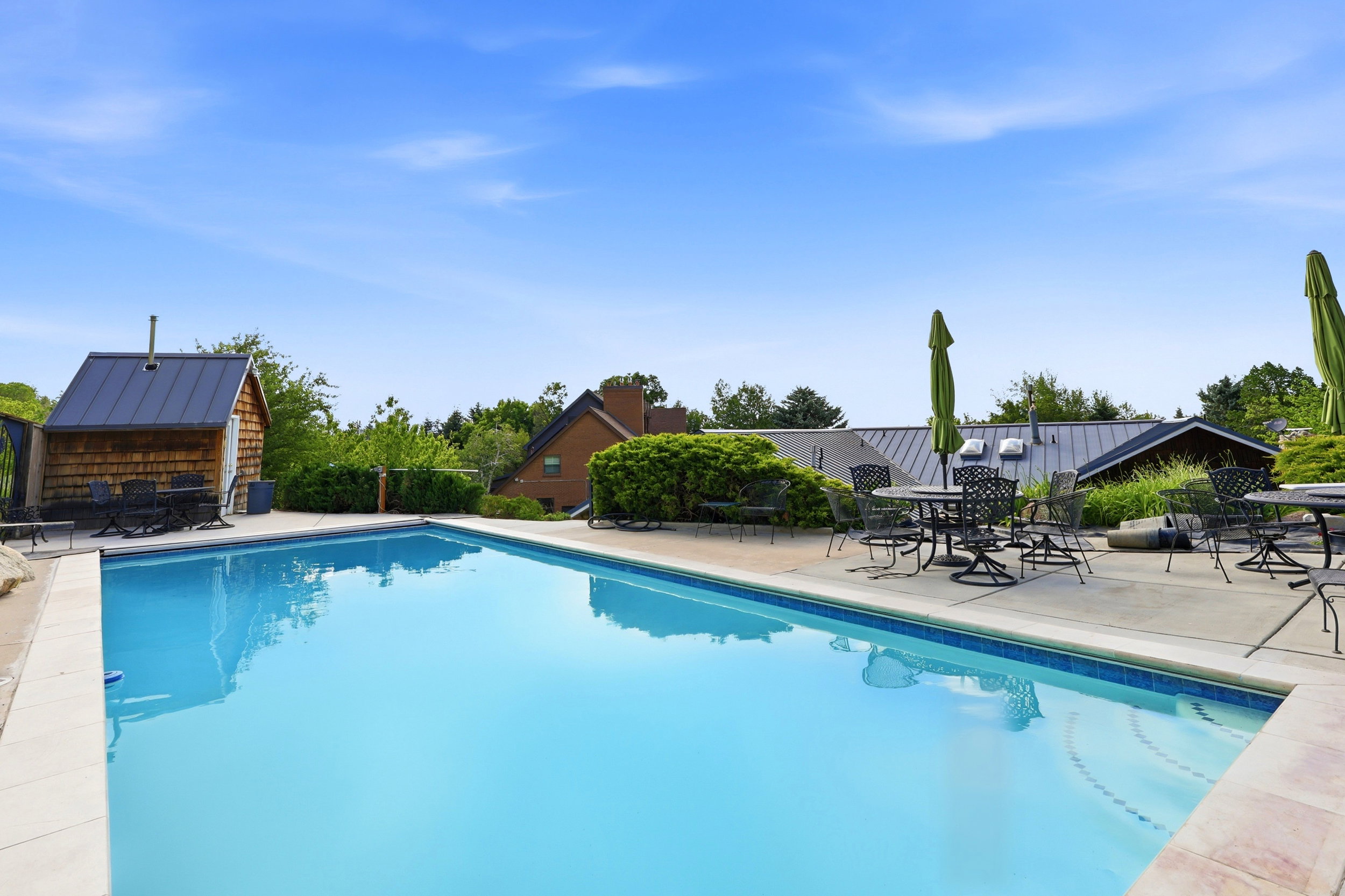 Outdoor swimming pool with a surrounding stone patio and a shingled pool house featuring a metal roof