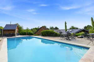 Outdoor swimming pool with a surrounding stone patio and a shingled pool house featuring a metal roof