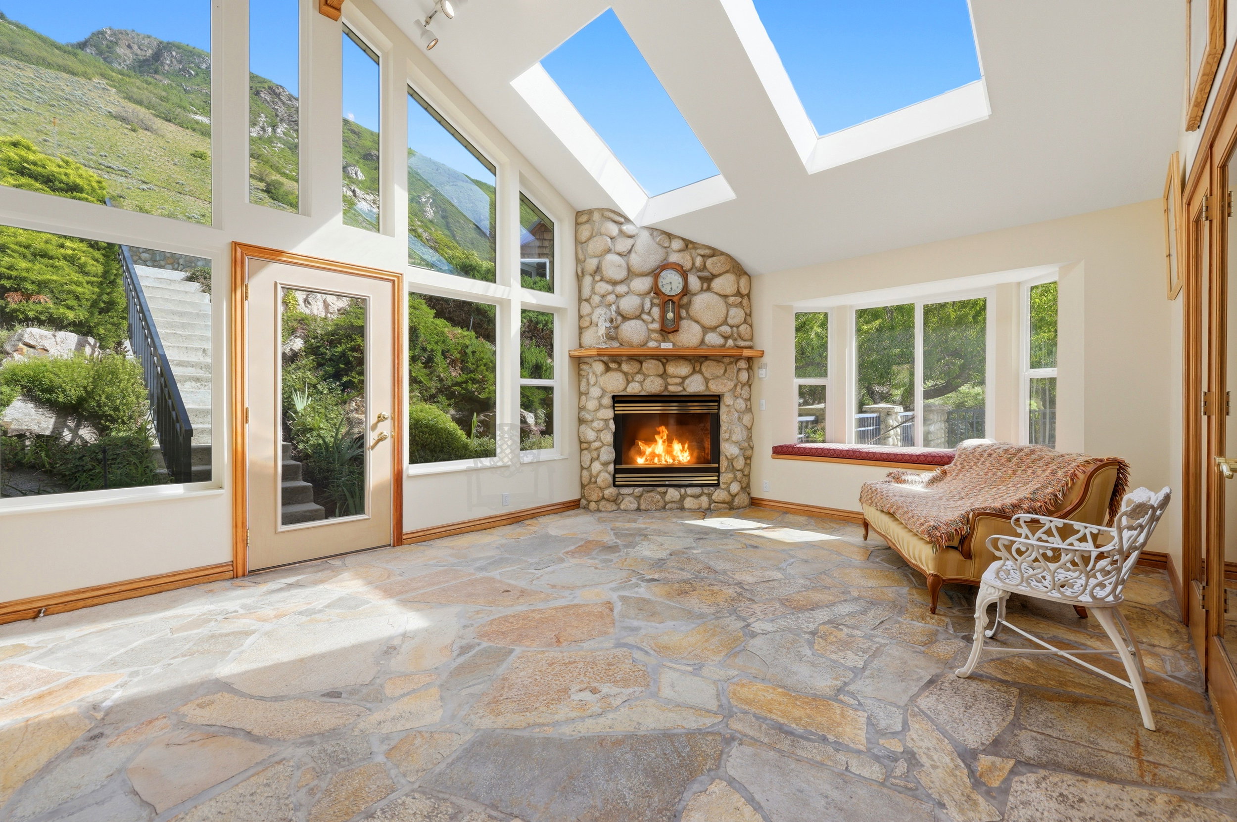 Stone flooring with an irregular pattern, a prominent stone-clad fireplace, and extensive windows showcasing an exterior landscape