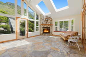 Stone flooring with an irregular pattern, a prominent stone-clad fireplace, and extensive windows showcasing an exterior landscape