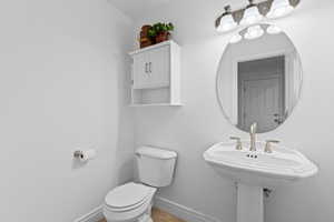 Powder room featuring a pedestal sink, oval mirror, and wall-mounted storage cabinet