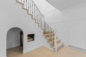 Staircase featuring carpeted treads, wrought iron balusters, and a paneled accent wall