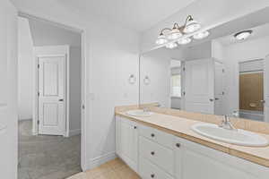 Bathroom featuring a dual vanity with white cabinetry, integrated sinks, and a tiled countertop