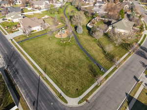 Expansive green space featuring a paved walking path, mature trees, and a playground area with a slide and climbing features
