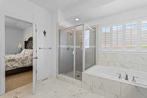 Bathroom featuring a glass-enclosed shower, a built-in soaking tub with marble-look tile surround, and white plantation shutters