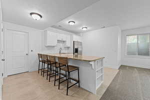 Kitchen space featuring white cabinetry, a light-toned stone countertop island with integrated shelving, and a stainless steel refrigerator