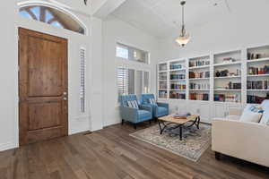 Foyer and living area featuring a solid wood entry door with an arched transom, wood-finish flooring, built-in white cabinetry with open shelving, shuttered windows, and a coffered ceiling