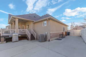 Rear exterior featuring a covered deck, direct concrete patio access, stucco siding, and a privacy fence