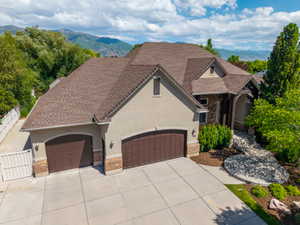 Stucco and stone facade home featuring a multi-car garage with arched doors, an expansive concrete driveway, and a covered entry with timber accents