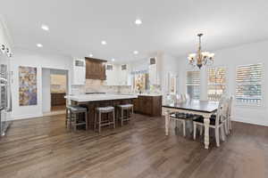 Open concept kitchen and dining area featuring wood-finish flooring, a central island with a light-colored countertop, white upper cabinetry, and dark wood-finish lower cabinetry