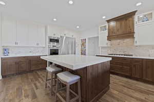 Kitchen featuring a large central island with seating, wood-finish flooring, white upper cabinetry, and dark wood-finish lower cabinetry