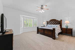Spacious interior featuring a bay window with plantation shutters, wall paneling, and a ceiling fan with integrated lighting