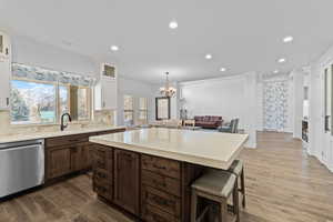 Gourmet kitchen featuring a large central island with seating, stainless steel dishwasher, wood-finish flooring, and upper white cabinetry with glass inserts