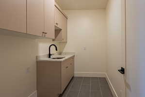Utility room featuring extensive cabinetry, a built-in sink with matte black gooseneck faucet, light-toned countertop, and large format floor tile