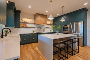 Modern kitchen featuring rich teal cabinetry, light wood-finish flooring, and white countertops