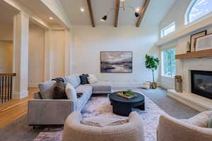 Vaulted ceiling featuring exposed beams, a white brick fireplace with a wood mantel, and multiple windows including an arched upper window