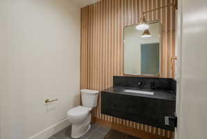 Floating vanity with dark countertop and integrated sink, complemented by a gold-framed mirror and wall-mounted sconce