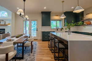 Open-concept kitchen and dining area featuring rich teal cabinetry, light wood-finish flooring, and a substantial island with seating