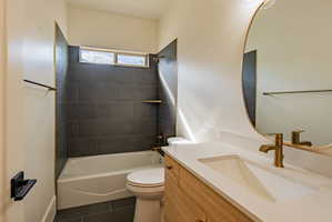 Bathroom featuring a built-in tub and shower combination with dark tile surround, a wood-finish vanity with an integrated sink, a light countertop, and an oval mirror