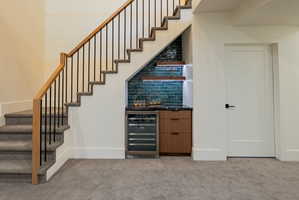 Custom under-stair bar featuring teal subway tile backsplash, dark countertop, wood-finish cabinetry, and built-in beverage refrigerator