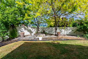 Manicured backyard featuring a flagstone patio, gravel landscaping, established trees, and a privacy fence