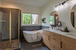 Contemporary bathroom featuring a freestanding soaking tub, a separate glass-enclosed shower with a pebble-tiled floor, a dual vanity with light wood-finish cabinetry, and twin oval mirrors