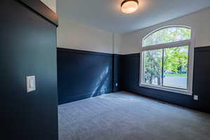 Room featuring a large arched window, two-tone wall treatment, textured carpet flooring, and a flush mount ceiling light fixture