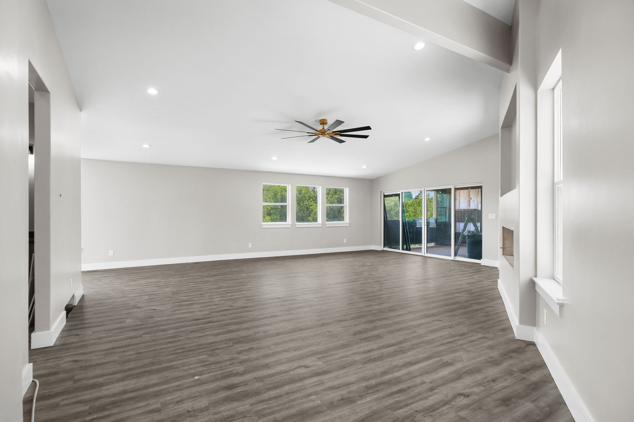 Spacious PRIMARY SUITE,  featuring vaulted ceilings, recessed lighting, a modern ceiling fan, wood-finish flooring, and multiple windows with sliding glass doors