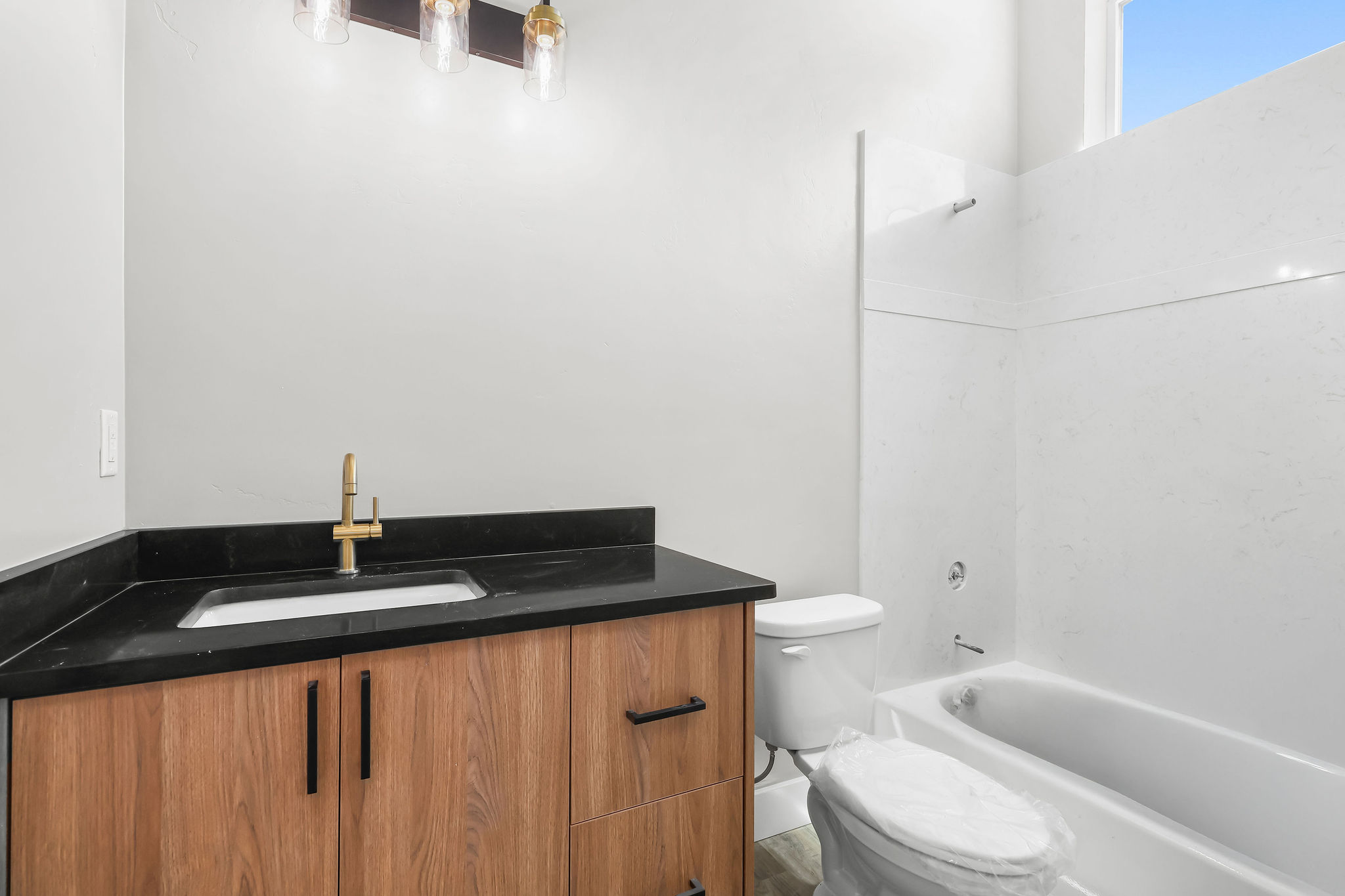 Bathroom featuring a wood-finish vanity with a black countertop and an undermount sink, a gold-tone faucet, and a three-light fixture