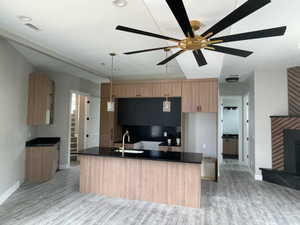 Open-concept kitchen featuring wood-finish cabinetry and a central island with a black countertop and integrated sink