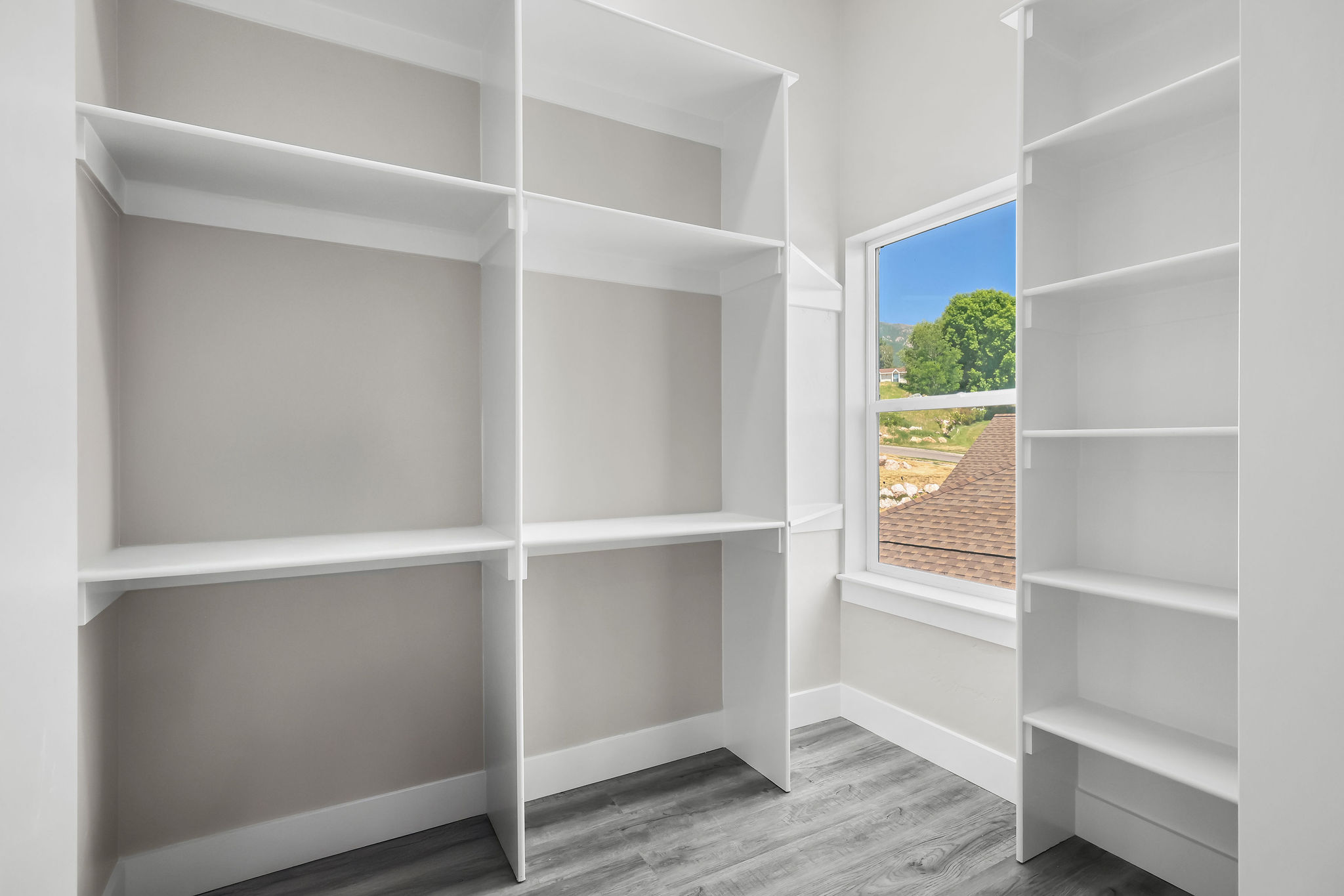 Room featuring extensive white built-in shelving, wood-finish flooring, and a window with white trim