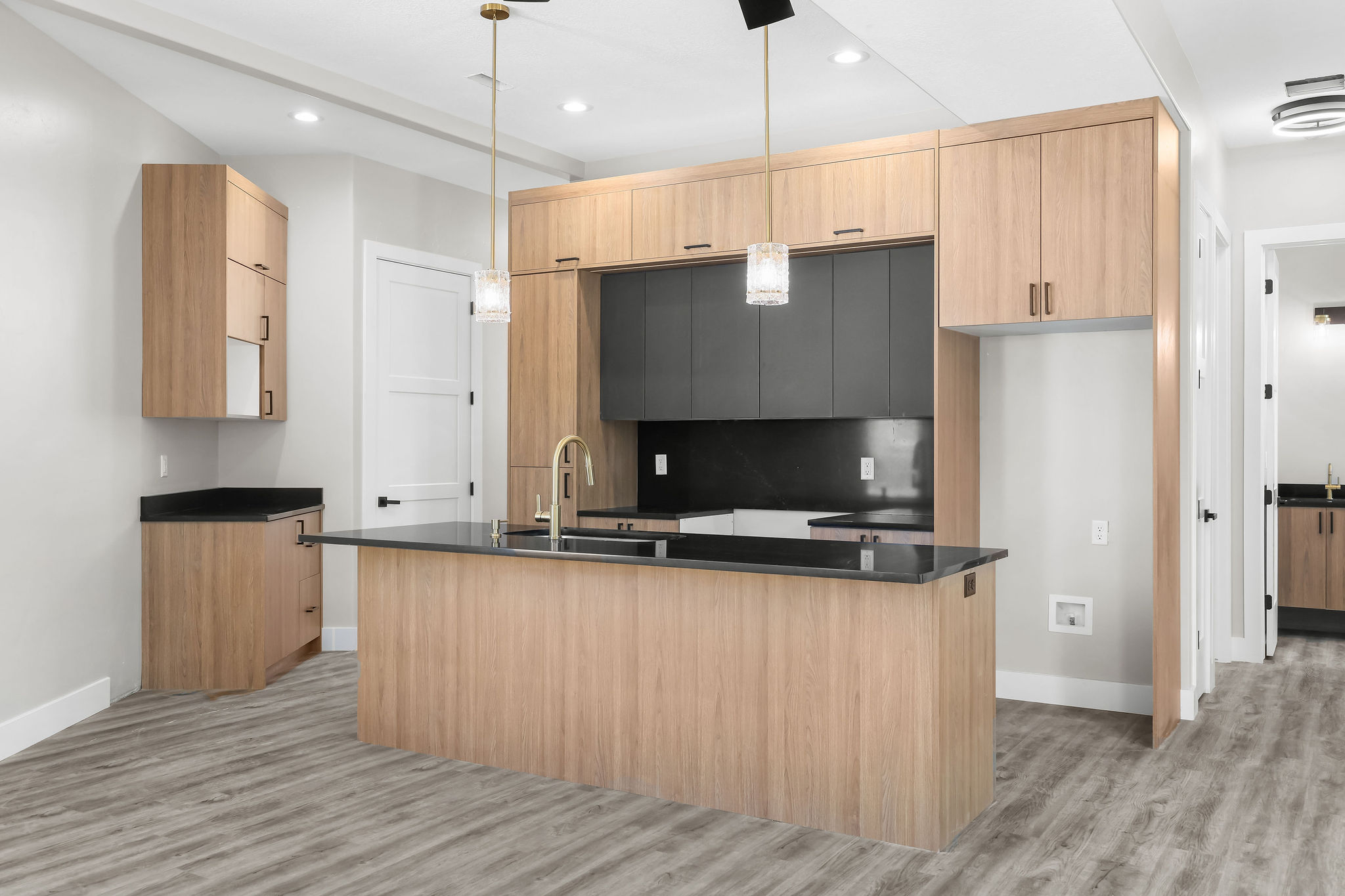 Modern kitchen featuring light wood-finish cabinetry, dark countertops, and a central island with a gold-finish faucet