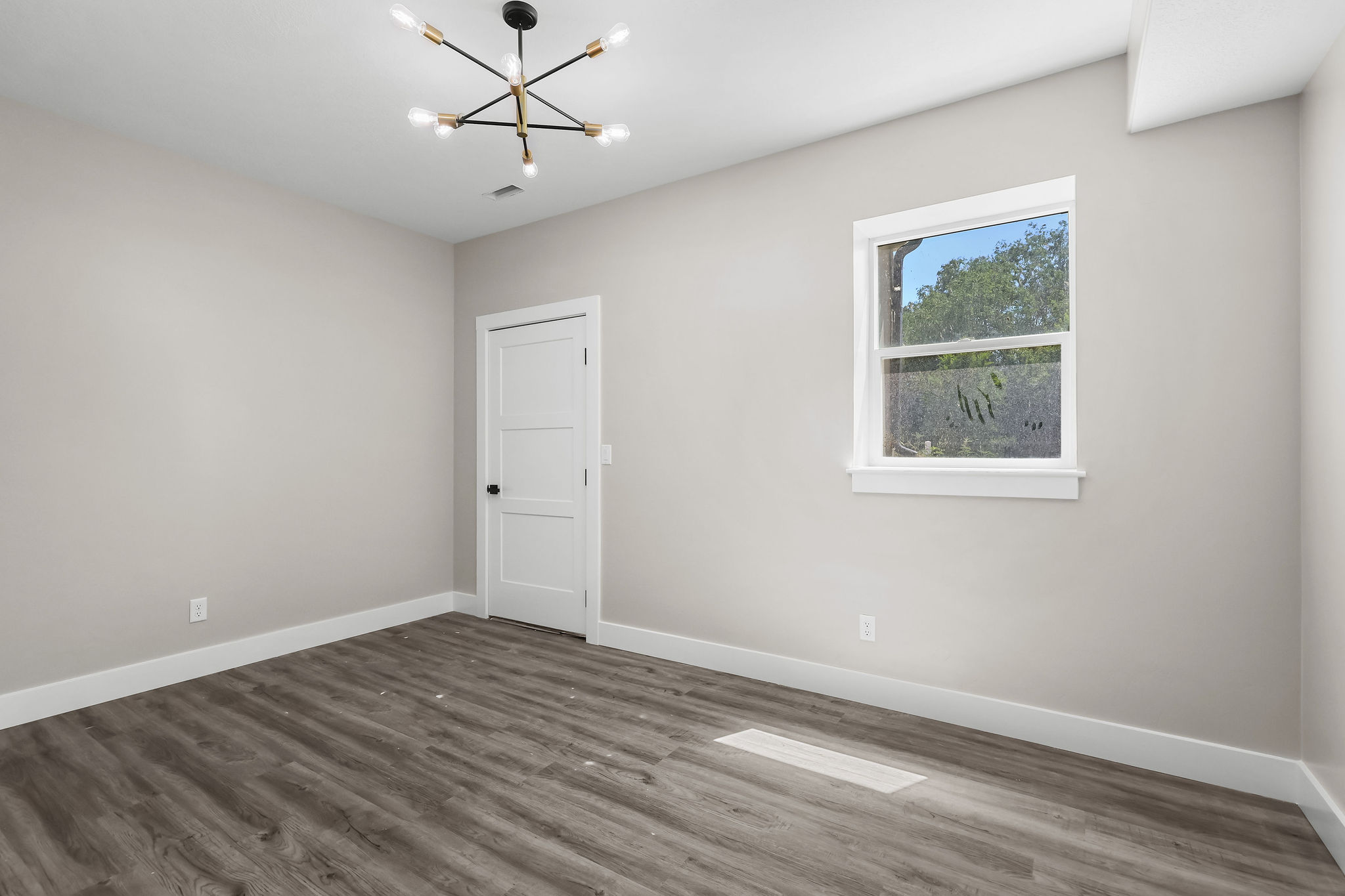 Spacious room featuring wood-finish flooring, light gray wall tones, a modern sputnik chandelier, white trim, and a white interior door