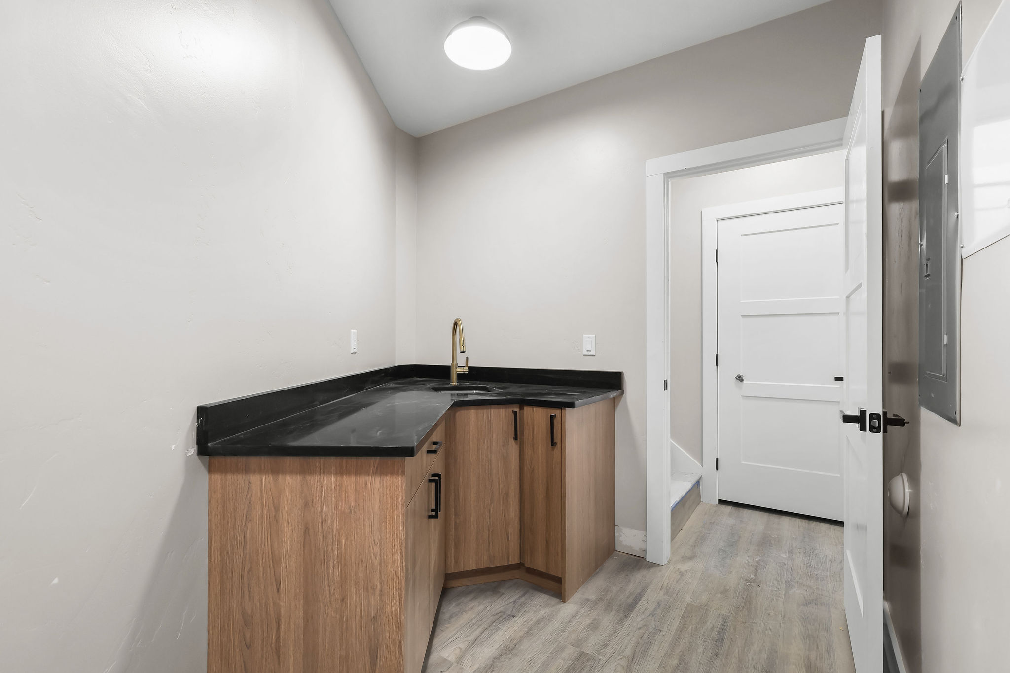 Corner wet bar featuring wood-finish cabinetry, dark countertops, and a gold-finish faucet