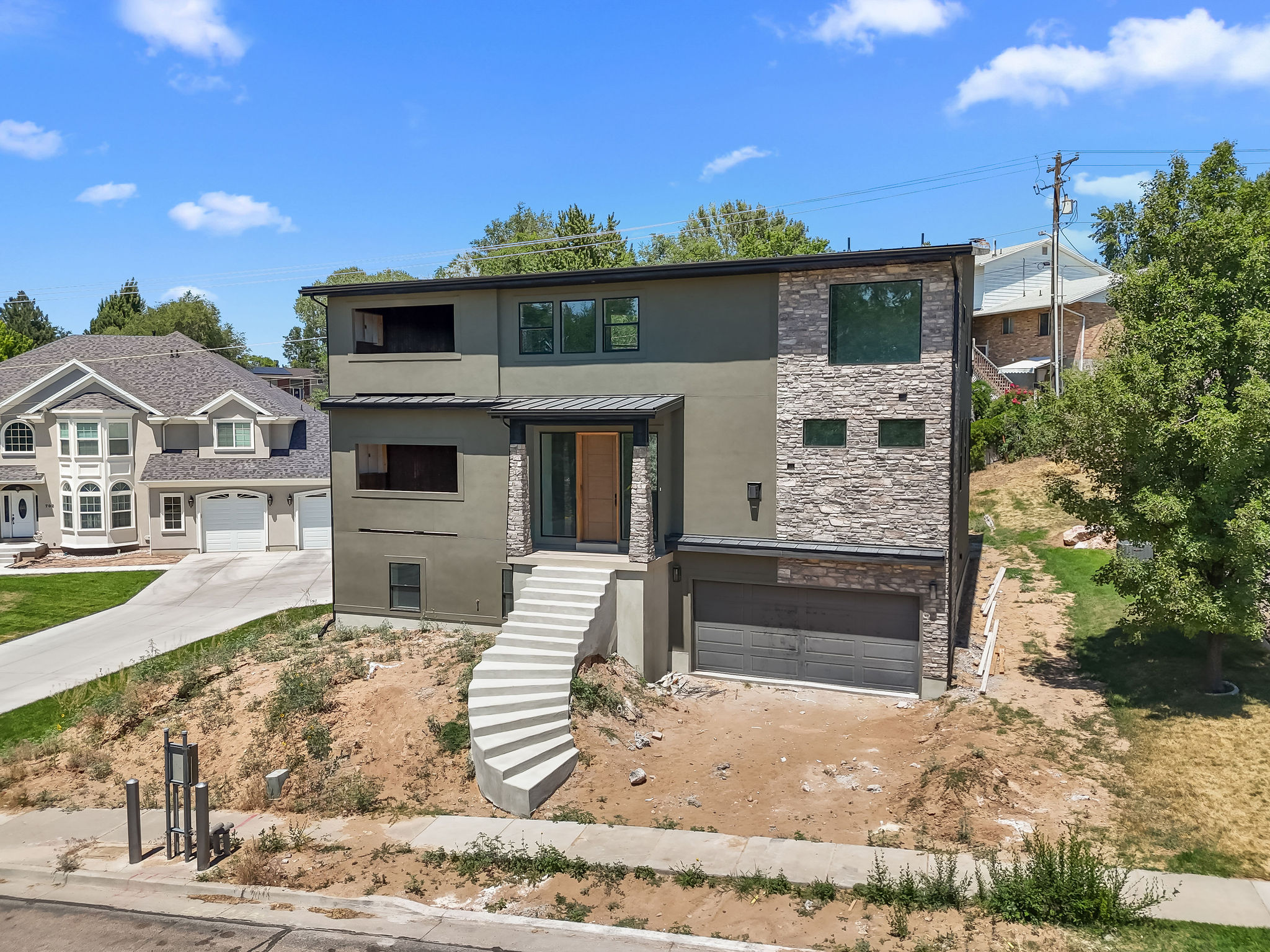 Modern multi-level residence featuring a gray and stone facade, flat roofline, and integrated garage