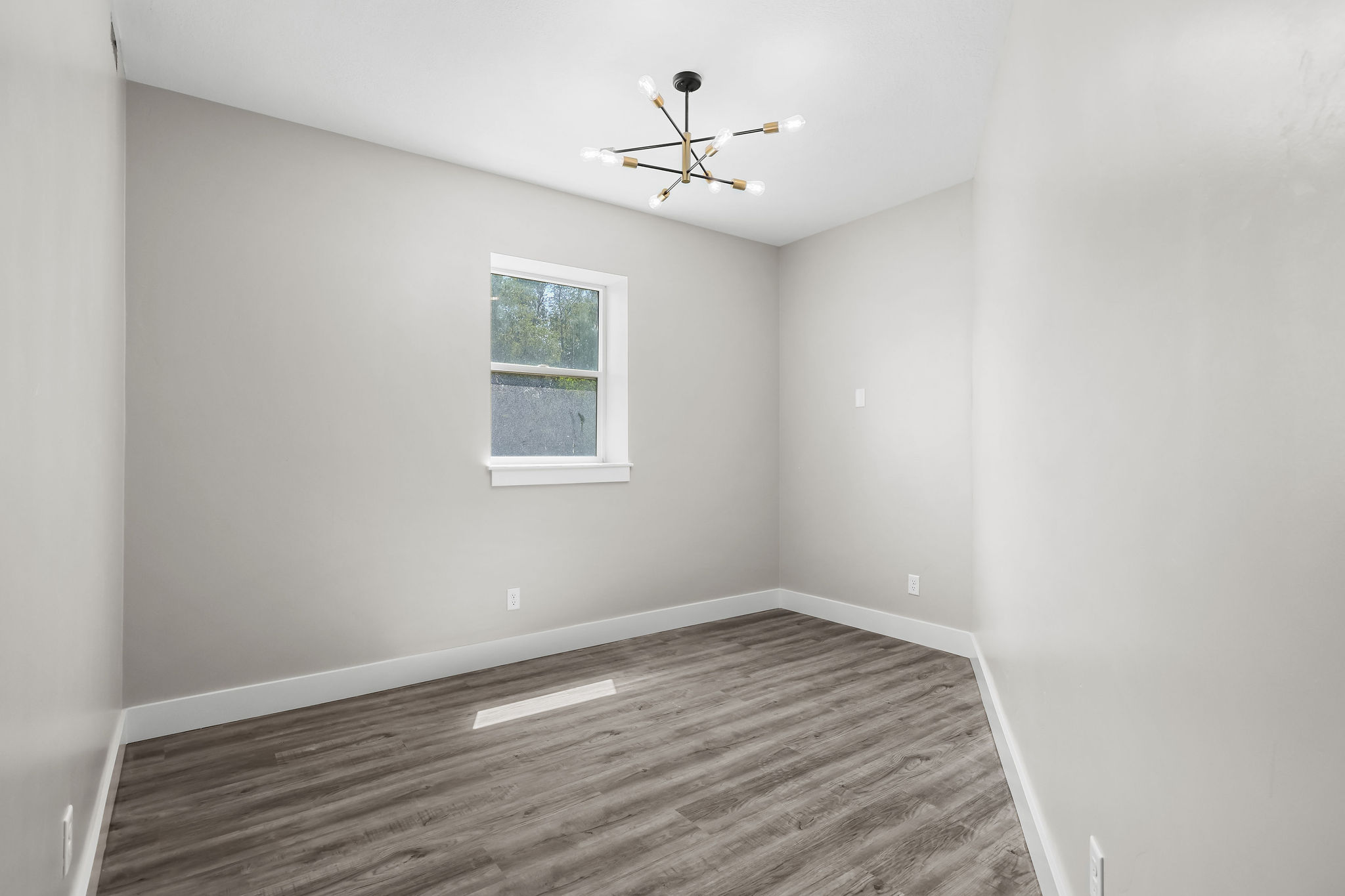 Room featuring wood-finish flooring, a modern chandelier with multiple exposed bulbs, and a window with white trim