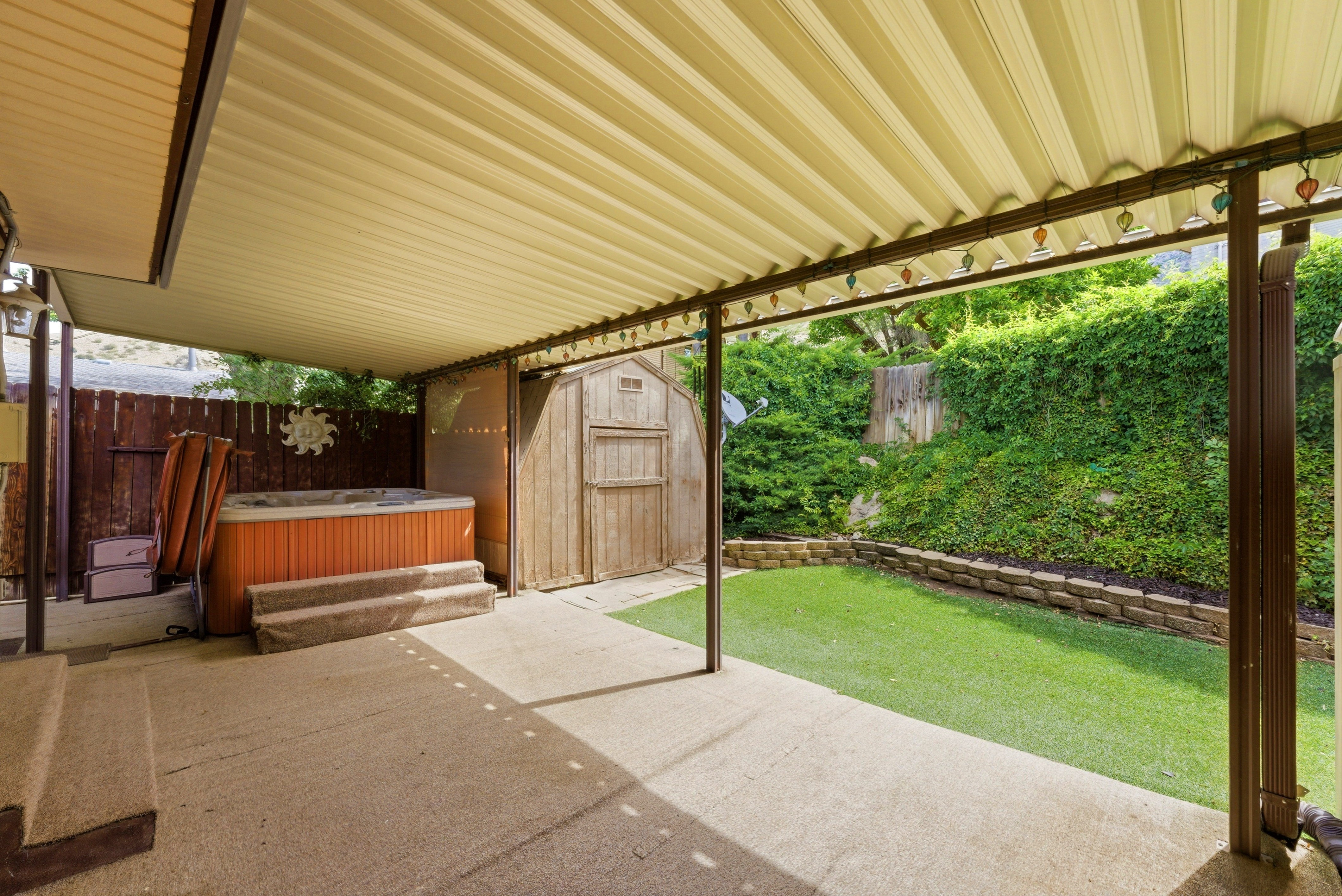 Expansive covered patio featuring a spa, concrete flooring, and a storage shed