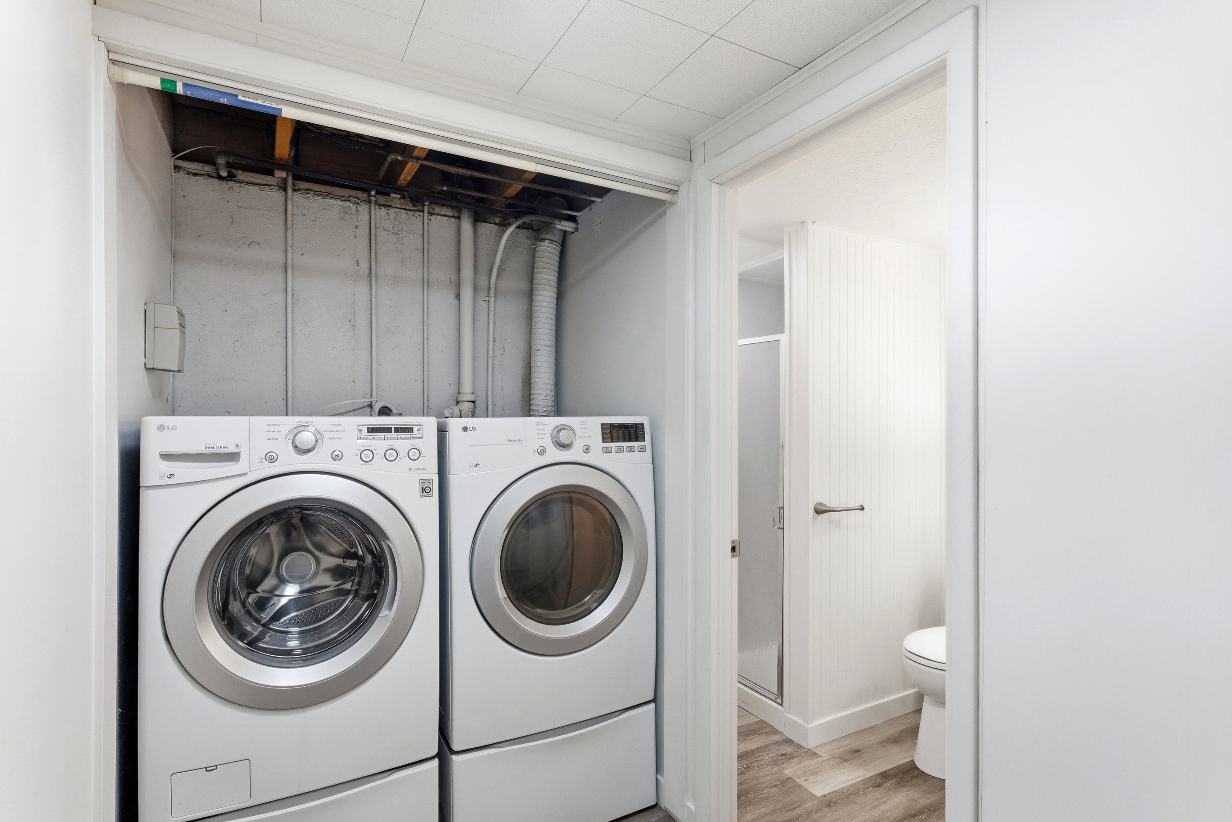 Dedicated laundry area with a front-load washer and dryer set, complemented by a nearby bathroom featuring wood-finish flooring, a toilet, and a glass-enclosed shower