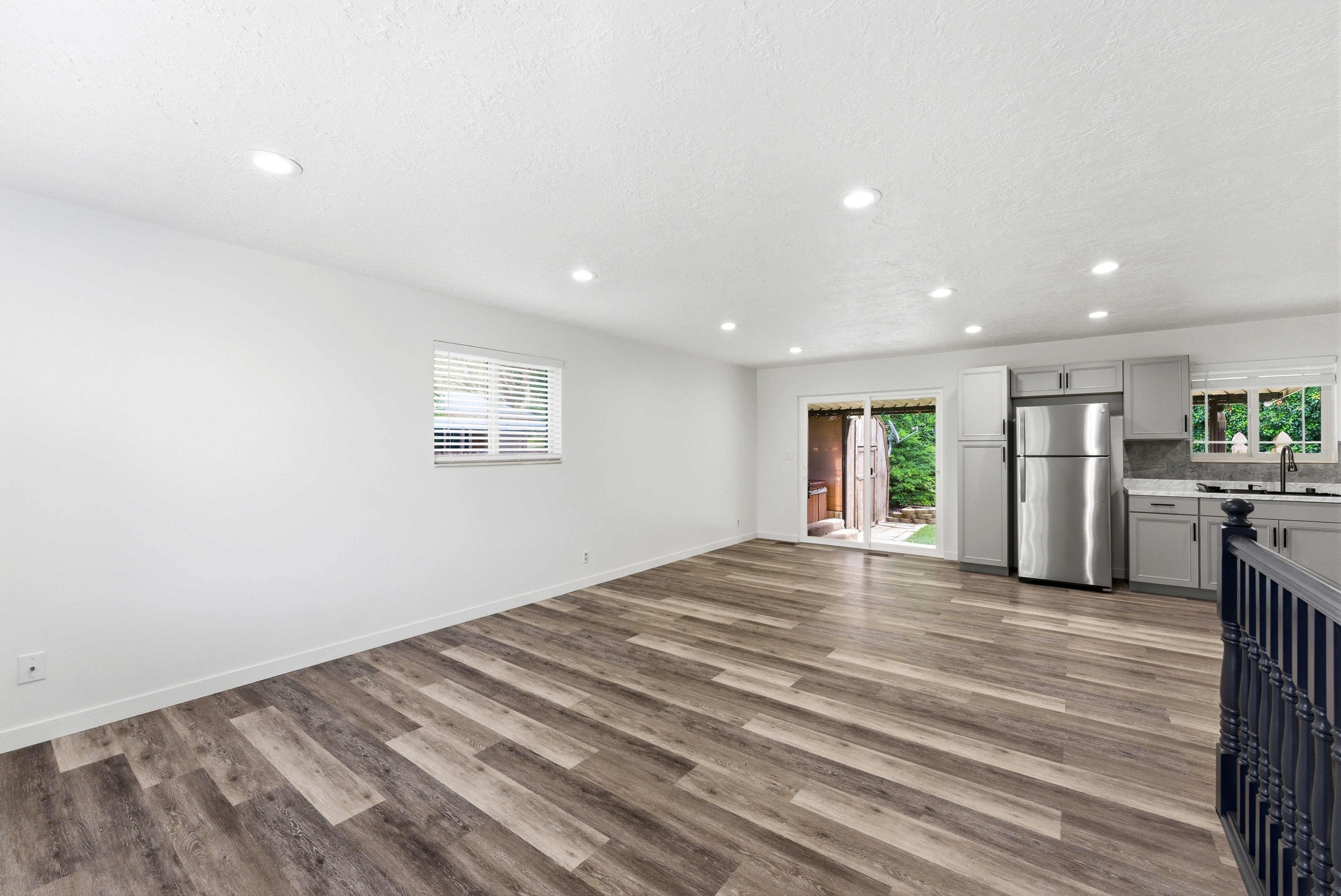 Open-concept living space featuring wood-finish flooring, recessed lighting, and a kitchen area with light gray cabinetry and stainless steel appliances