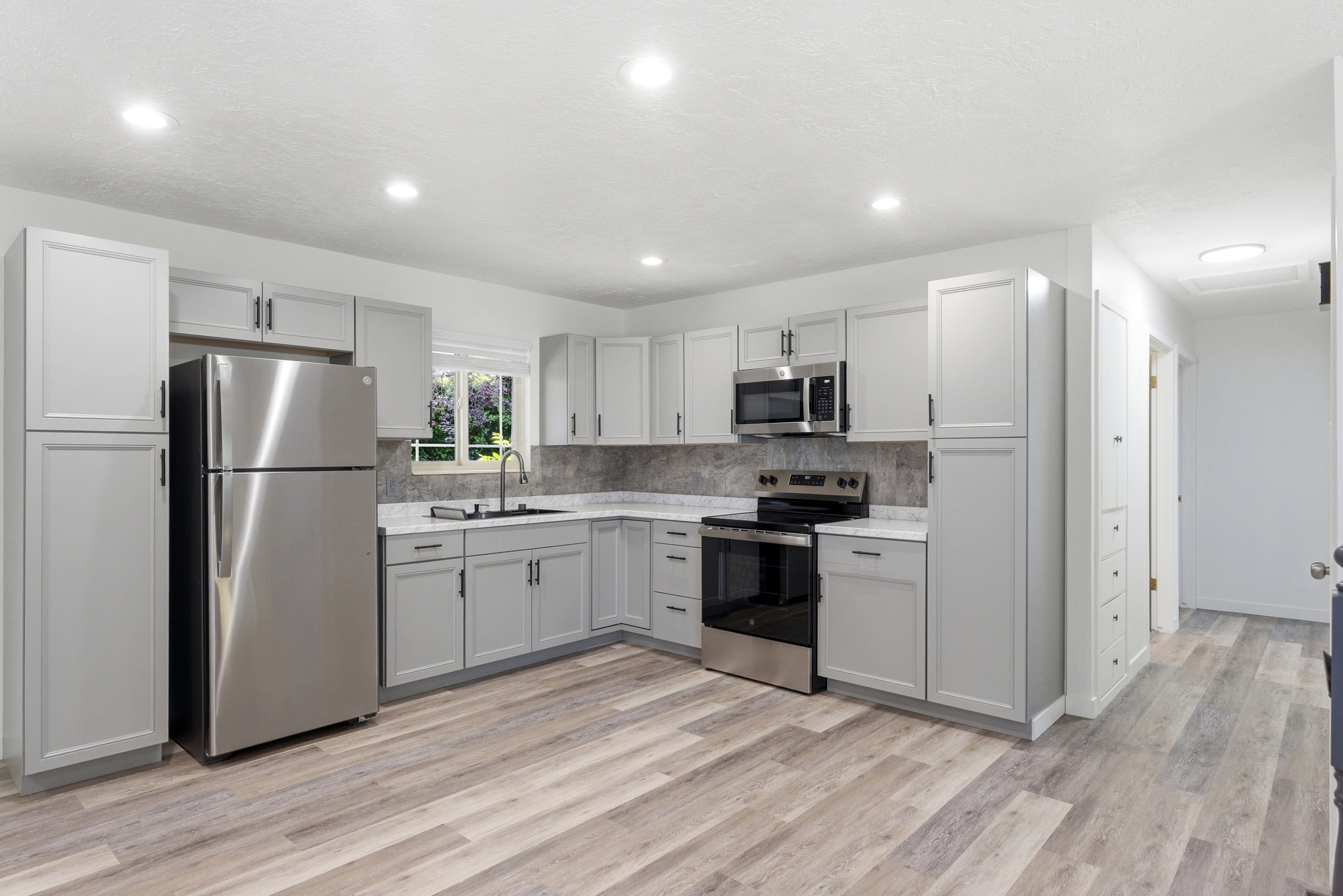 Modern kitchen featuring light gray cabinetry with black hardware, stainless steel appliances, and wood-finish flooring