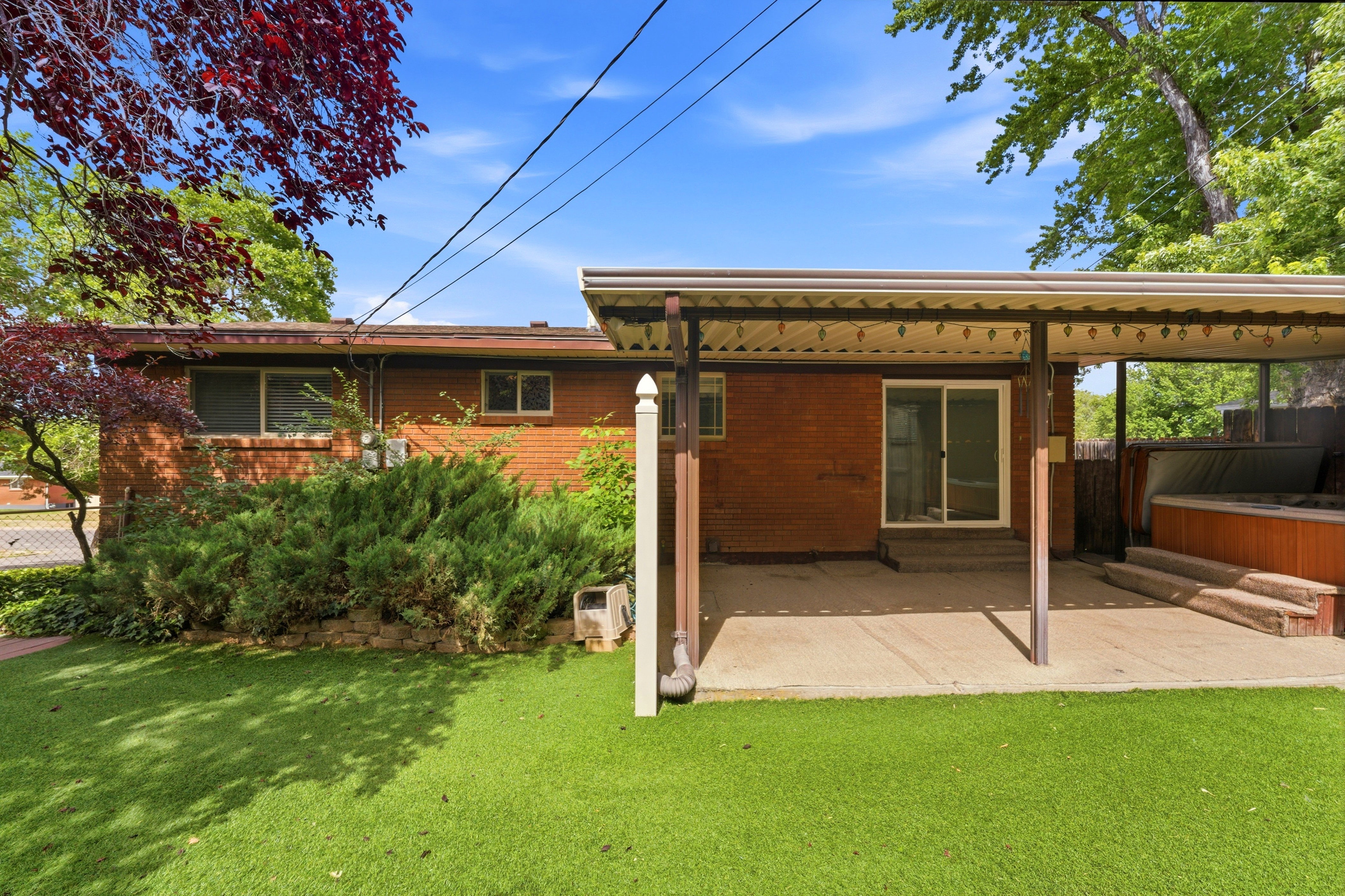 Brick exterior with covered patio, sliding glass door, and artificial turf lawn