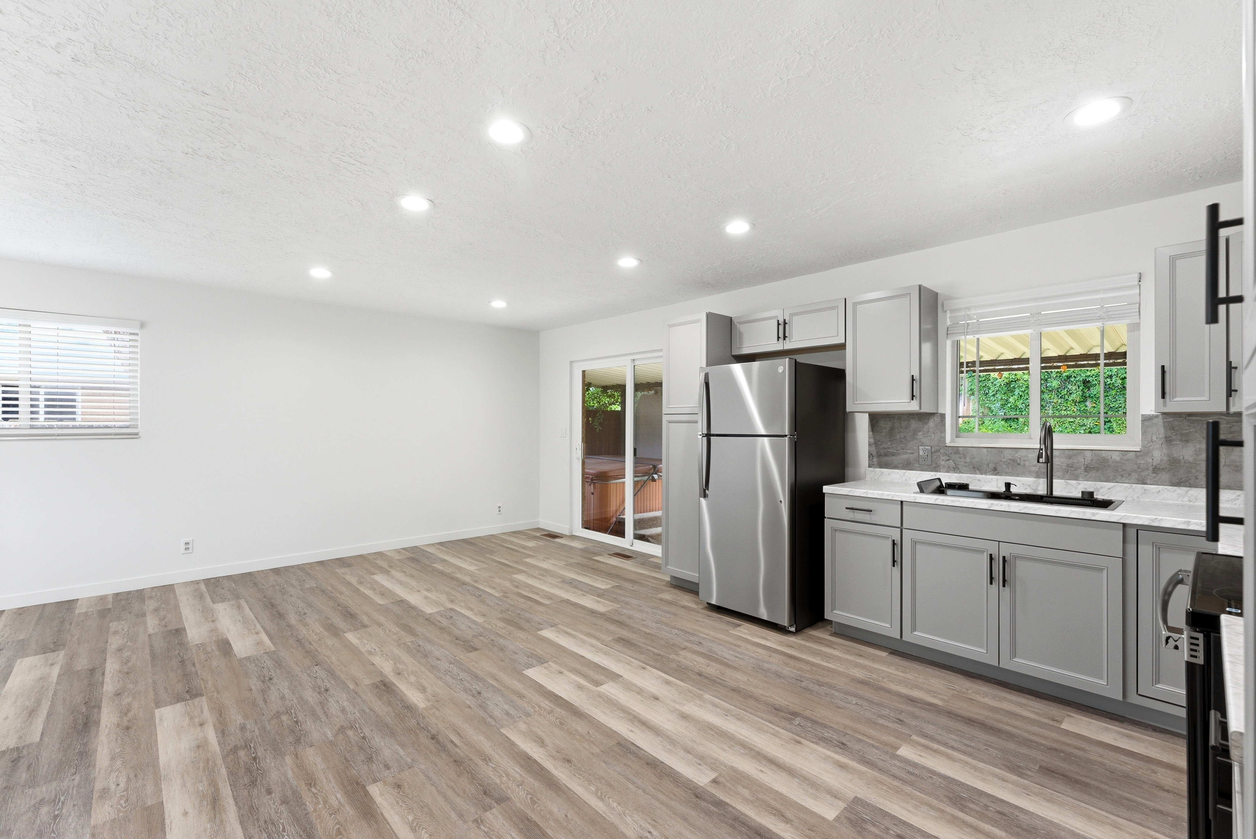 Open-concept living area featuring wood-finish flooring, recessed lighting, and a kitchen with gray cabinetry, a stainless steel refrigerator, and a sliding glass door