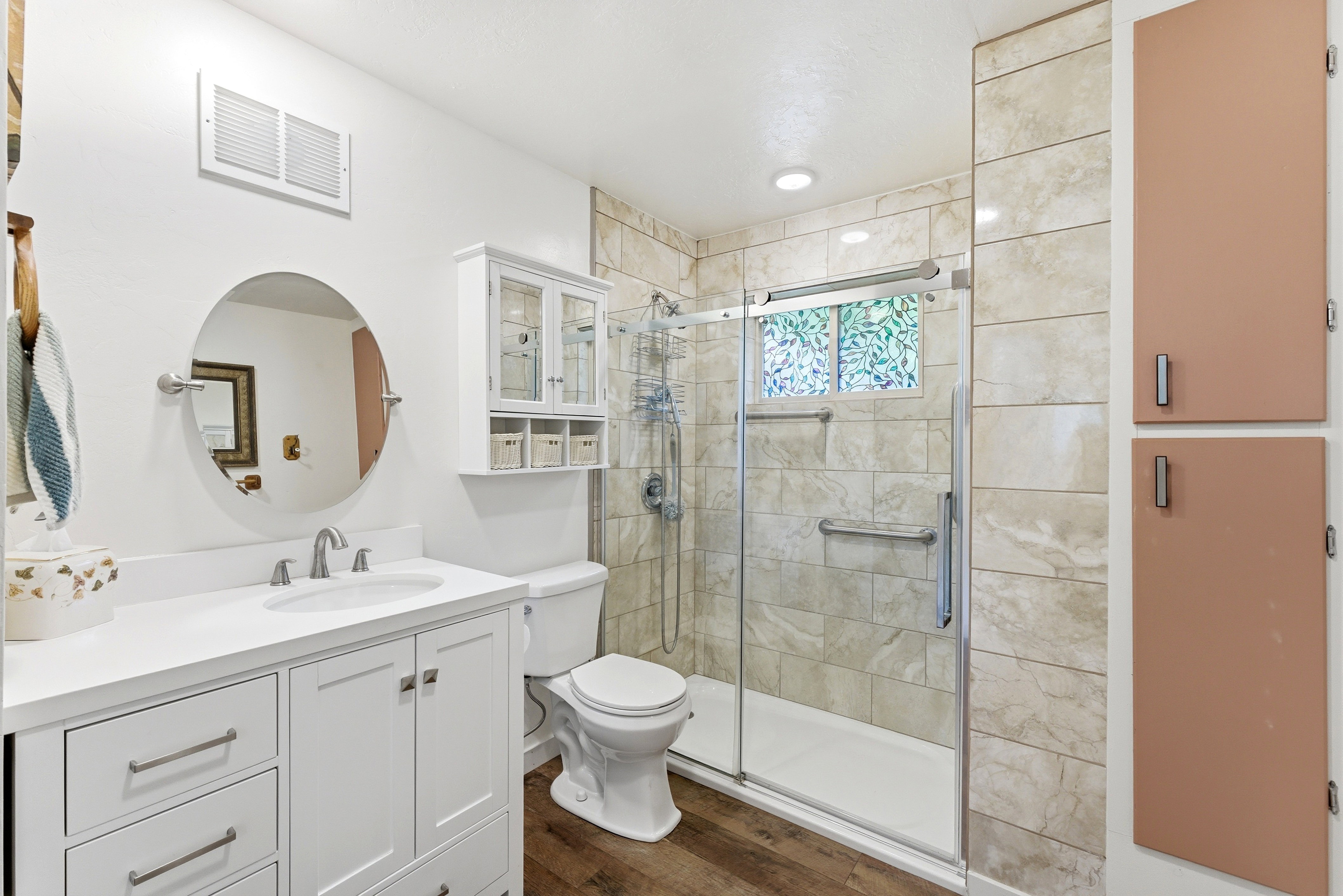 White vanity with a round mirror, stainless steel faucet, and undermount sink