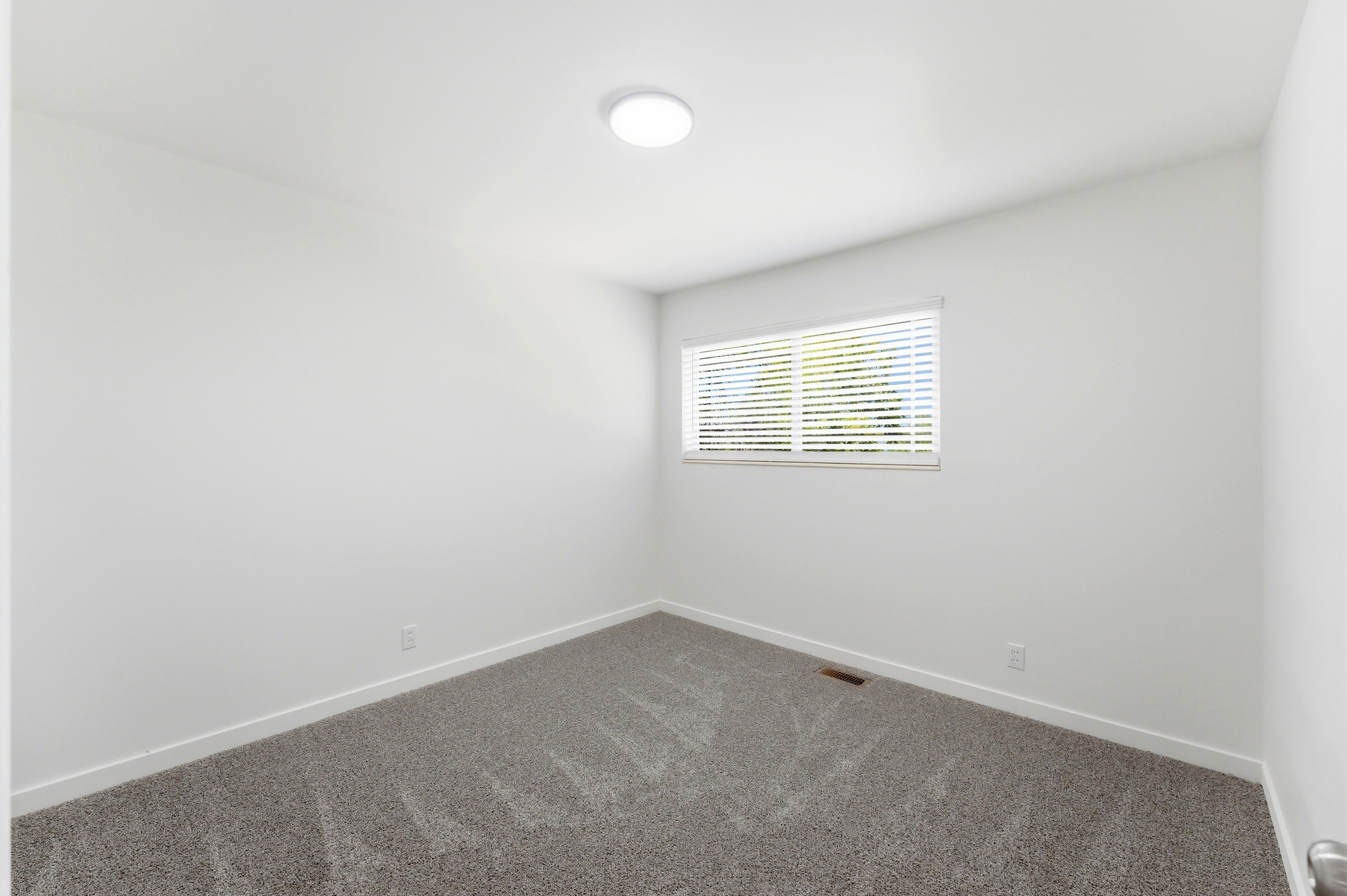 Room featuring light gray patterned carpeting, white baseboards, a single window with horizontal blinds, and a flush-mount ceiling light fixture