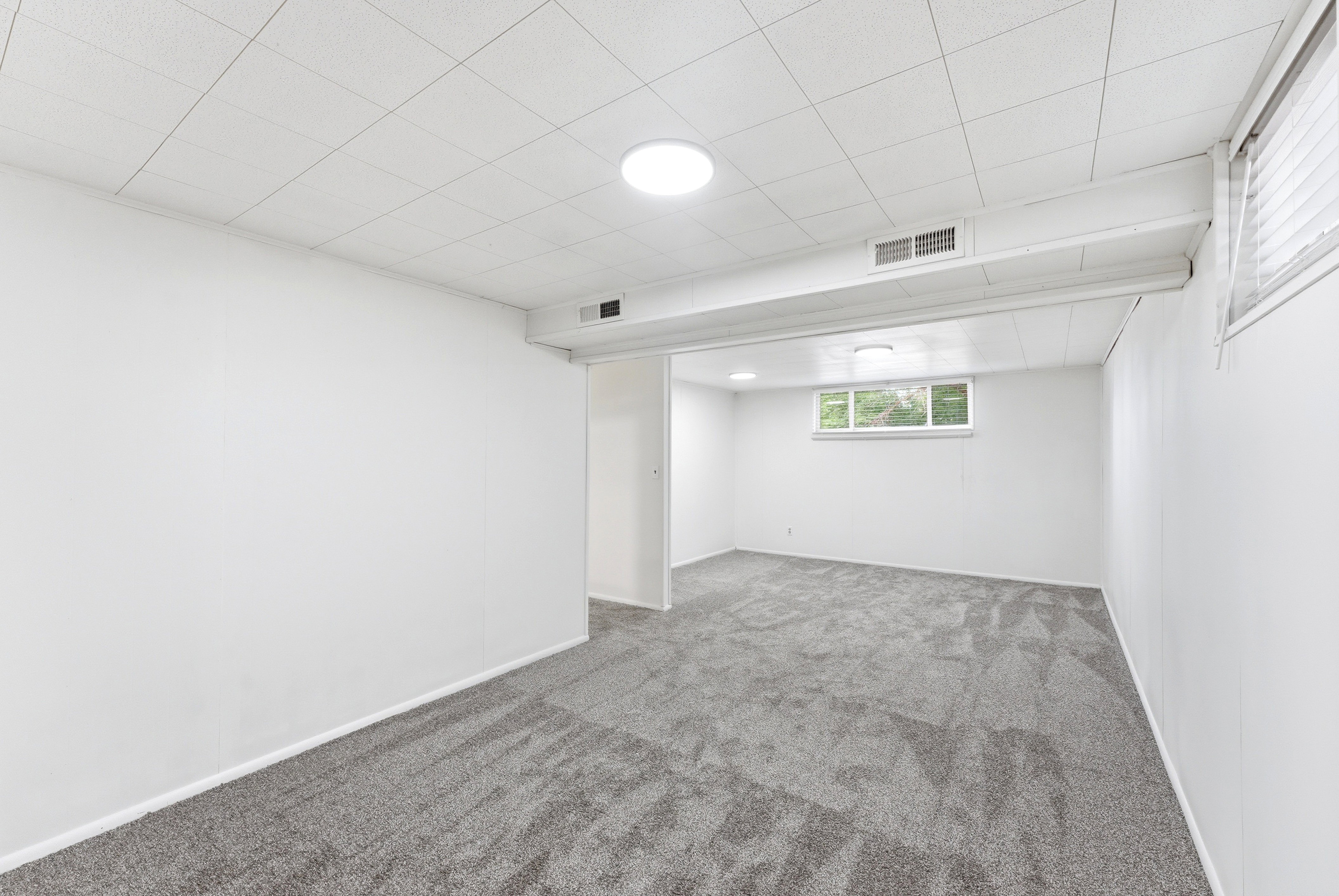 Spacious room featuring neutral gray carpet, white walls, and a drop ceiling with recessed lighting