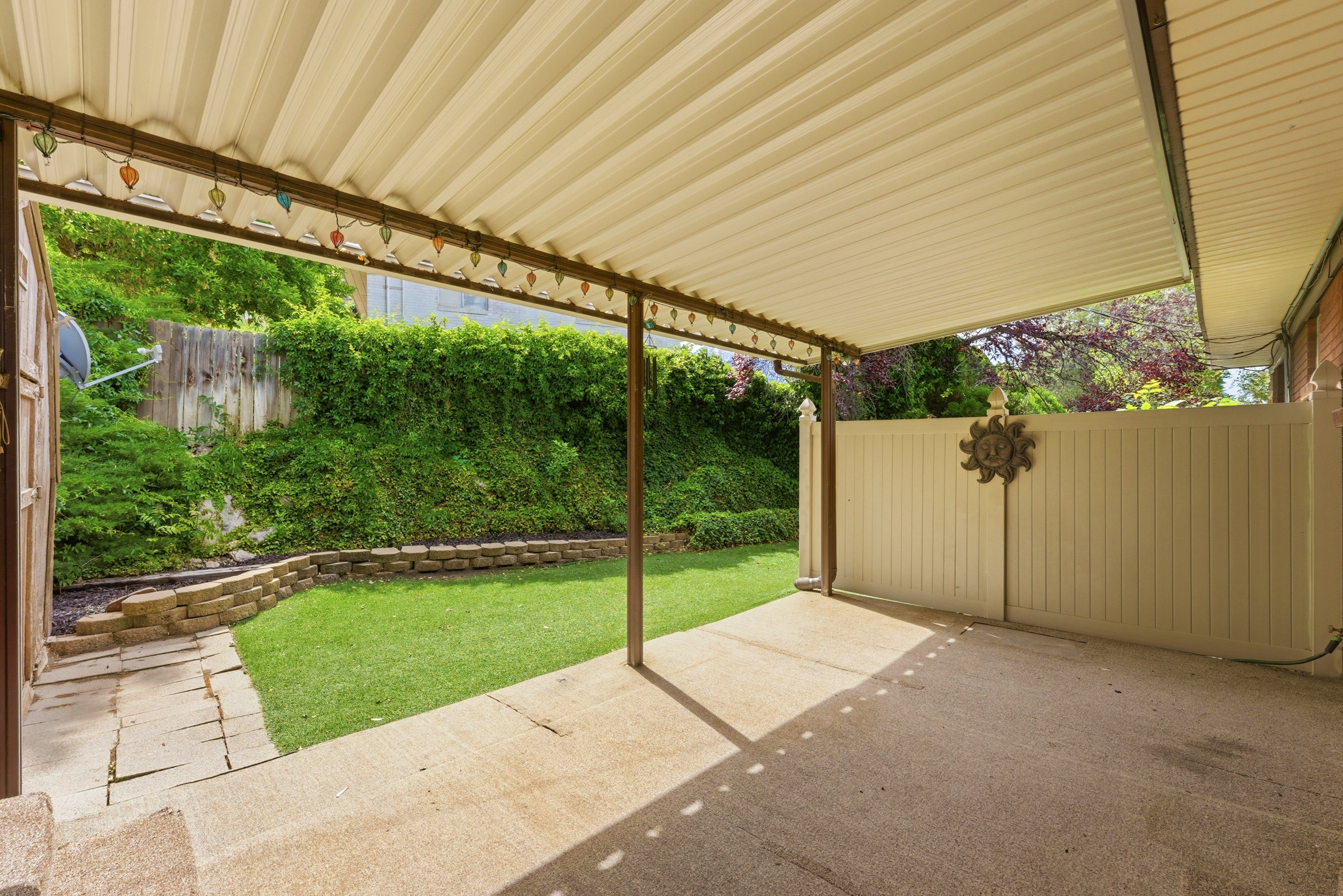 Covered concrete patio overlooking a terraced lawn area with mature landscaping and a privacy fence