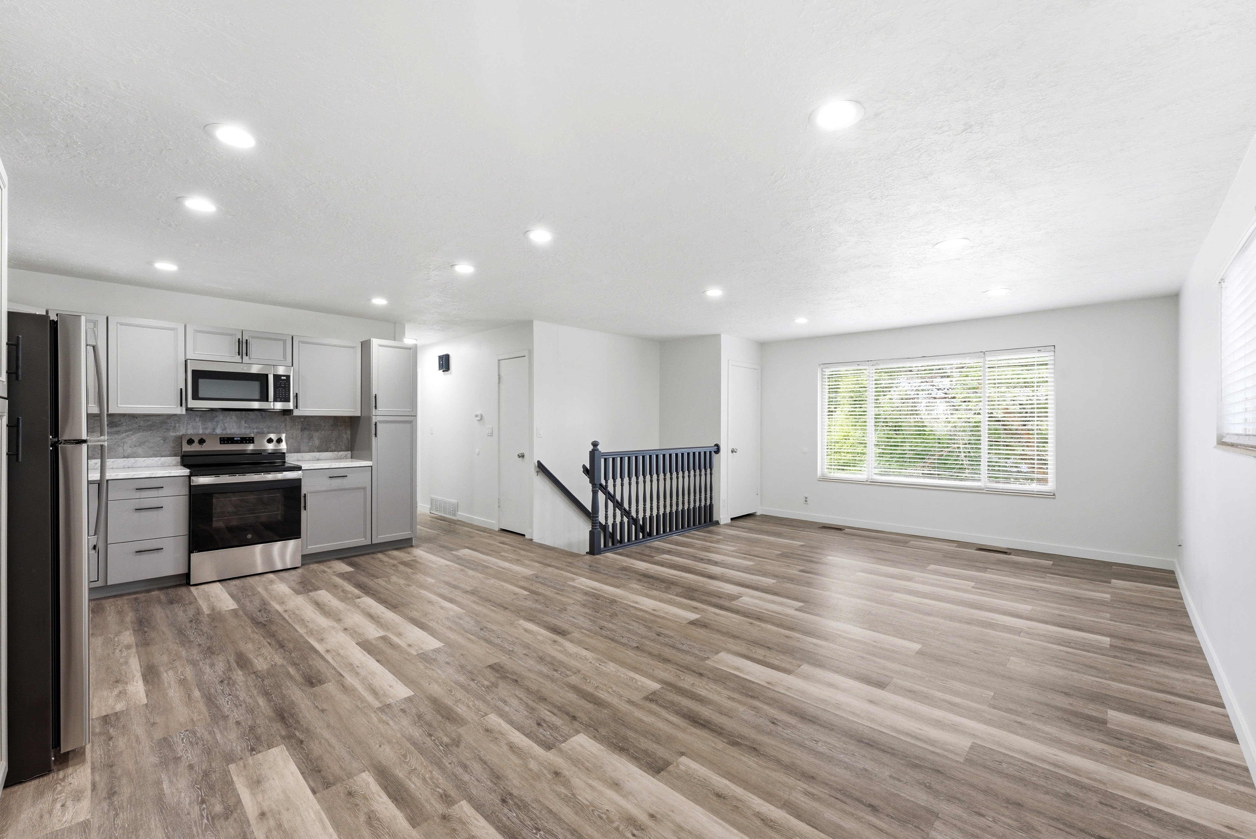Open-concept living space featuring wood-finish flooring, recessed lighting, and a kitchen with light grey cabinetry, stainless steel appliances, and a marble-finish backsplash