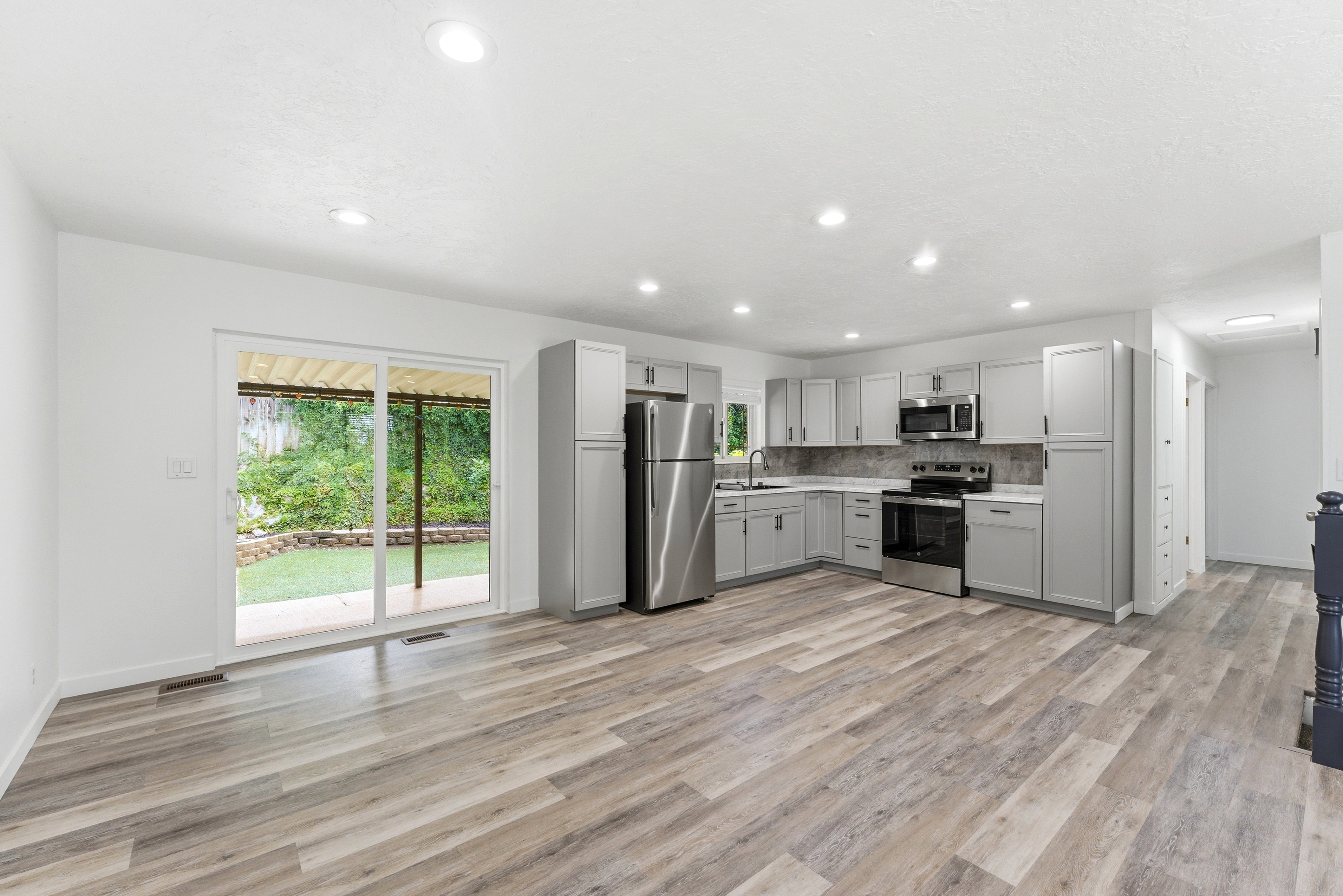 Open-concept living area featuring wood-finish flooring, recessed lighting, and a kitchen with gray cabinetry and stainless steel appliances