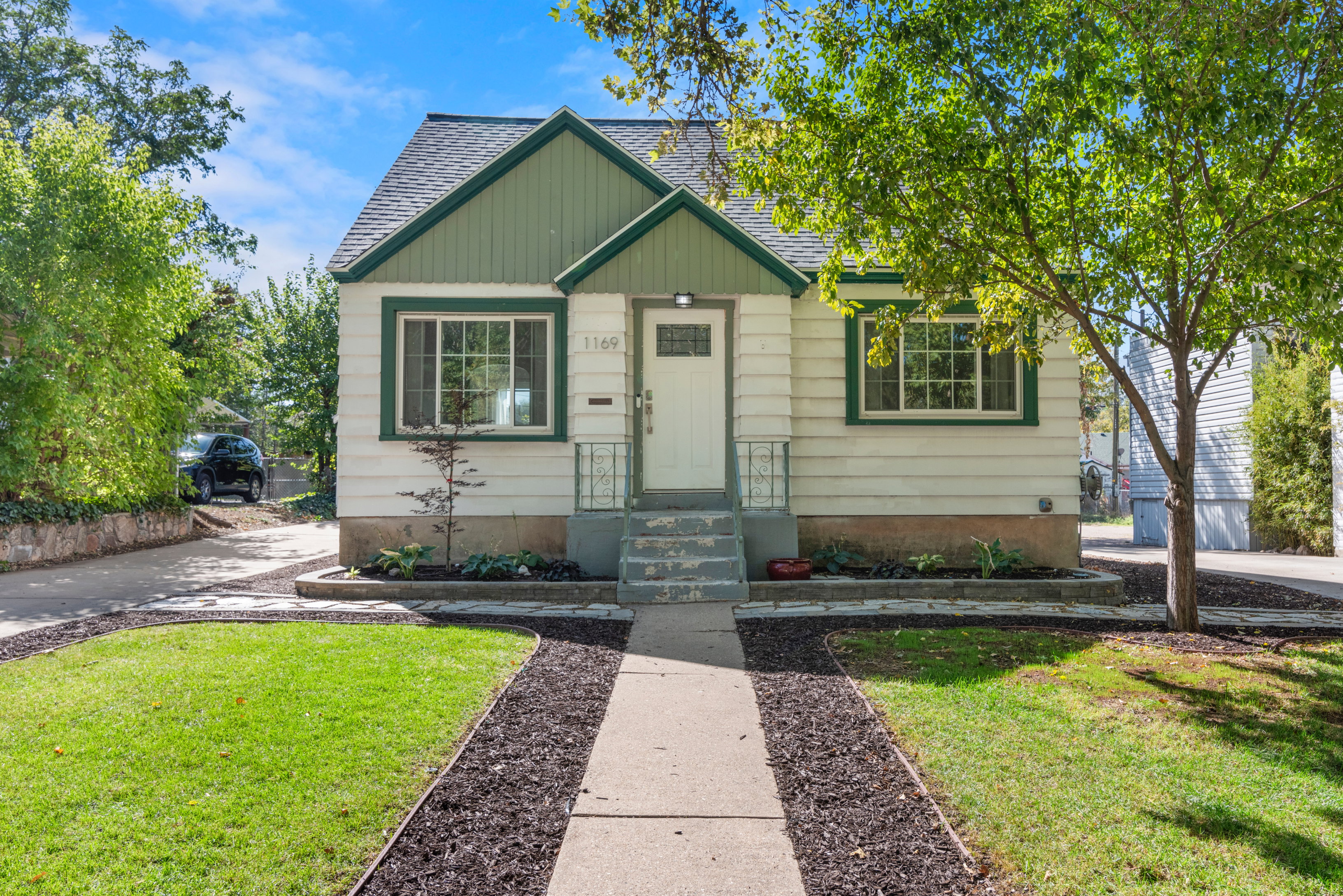 Charming single-family residence featuring a white and green exterior with front porch, well-manicured landscaping, and mature trees