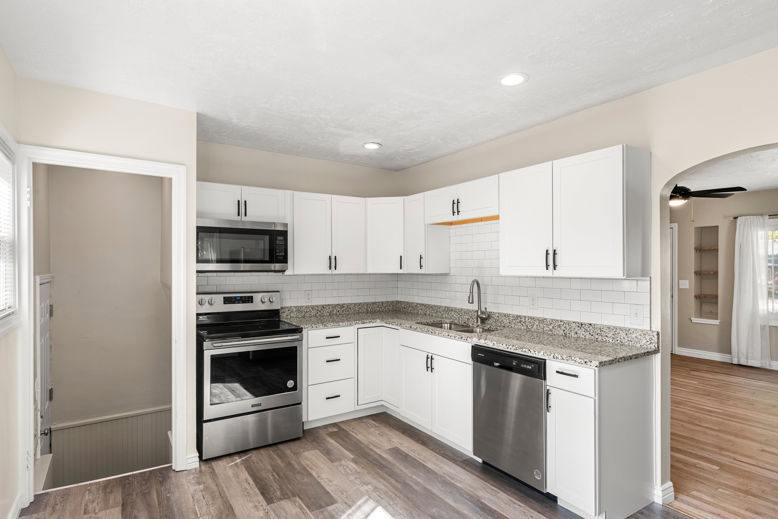 Remodeled kitchen featuring white cabinetry, granite countertops, subway tile backsplash, stainless steel appliances, and recessed lighting